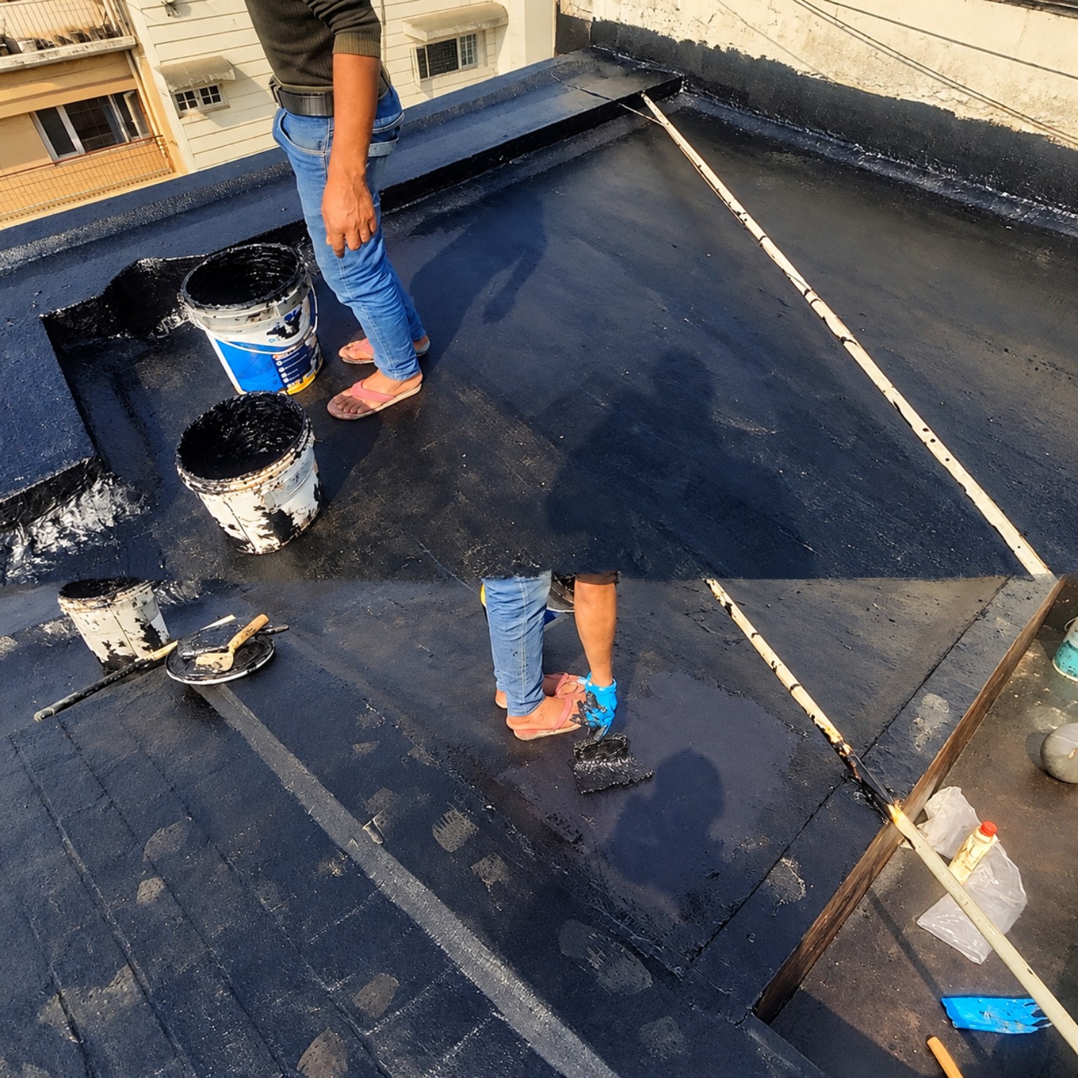 Black bituminous roof coating application in progress